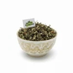 Dried Charila herb leaves (Parmelia Perlata / Pathar Phool) overflowing in a patterned white ceramic bowl with a small Pansar Essential flag.